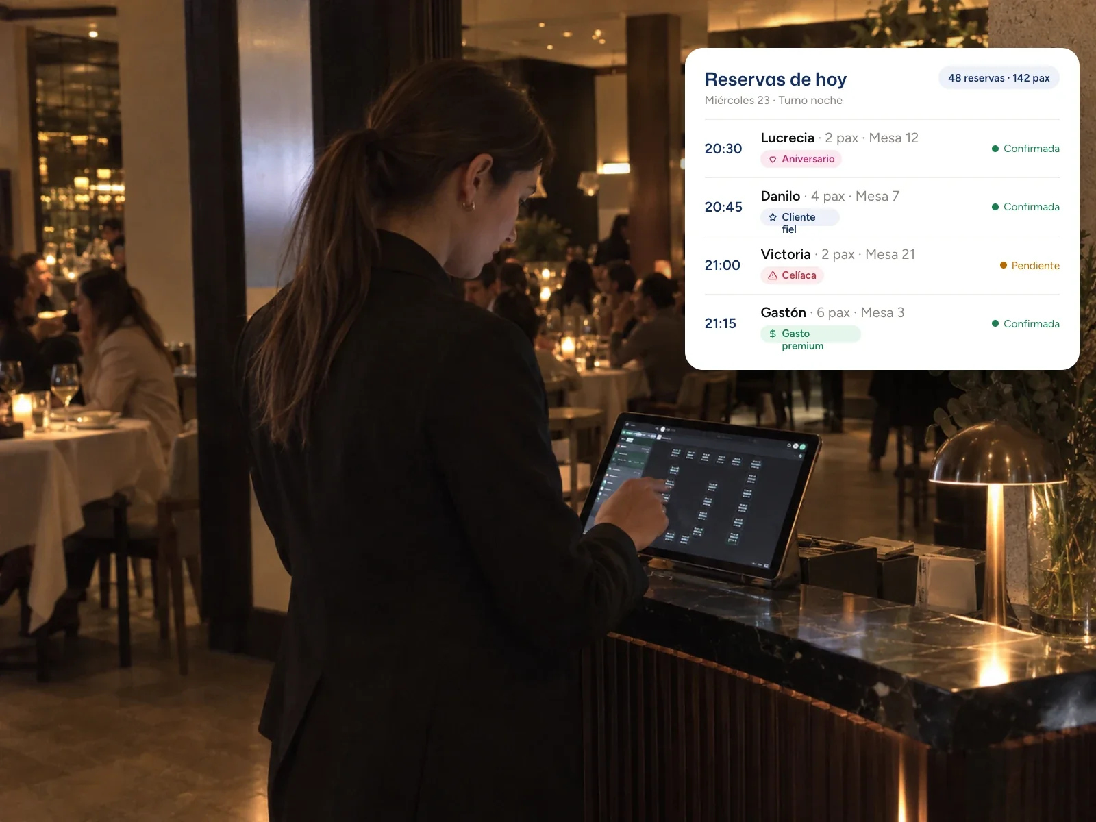 Anfitriona en la recepción del salón trabajando sobre el plano de mesas de Woki en una tablet, junto a la lista de reservas de la noche